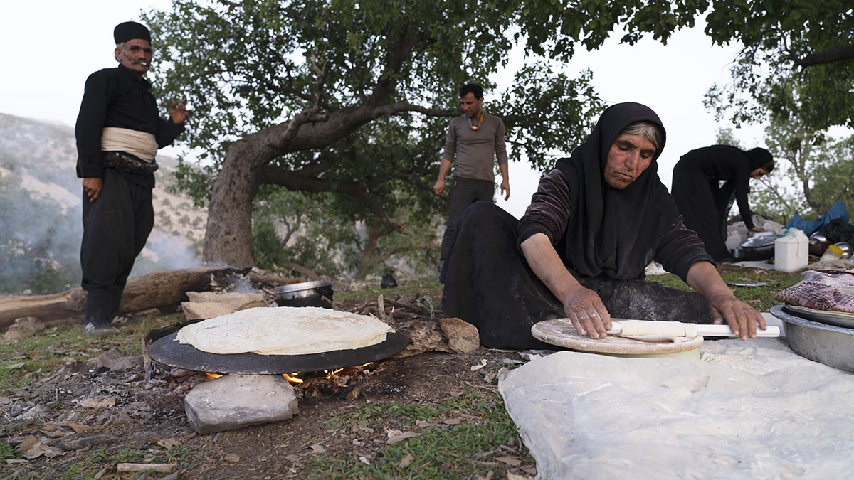A Bakhtiari nomad woman is making Tiri bread and the nomad man is standing by a tree in the Zagros area
